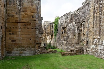 Stone ruin with moss-covered wall and grassy foreground; ancient silence echoes through fractured...