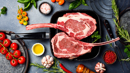 Raw Tomahawk Steak in a pan. Cooking Tomahawk steaks, spices, seasonings, butter and salt on a gray stone table.