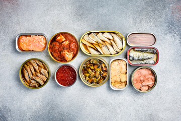 Top view of canned fish and seafood: tuna, salmon roe, sprats, cod liver and mackerel. On a light stone background.