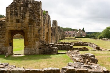 the ruins of an old stone structure with grass and a building in the background under a cloudy sky in Mount Grace Priory - East Harlsey - North Yorkshire - UK