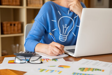 Businesswoman is working on a laptop and taking notes on a notepad, with a light bulb symbolizing a...