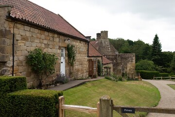 A quaint stone building with a red-tiled roof sits amidst green grass in Mount Grace Priory - East Harlsey - North Yorkshire - UK
