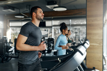 Man running on treadmill with group of people in modern gym