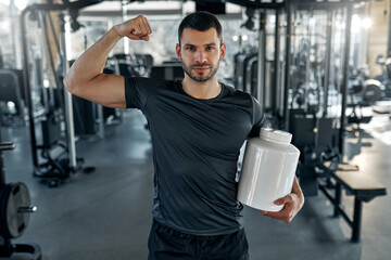Man showing biceps and holding blank protein jar in gym