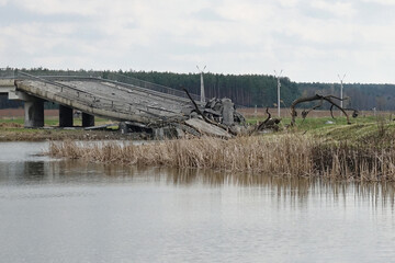 Collapsed modern concrete bridge over a calm body of water, showing significant structural damage
