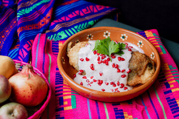 Classic Mexican chile en nogada served in a clay dish with fresh ingredients: apple, pear, walnut, and pomegranate over a vibrant textile background.
