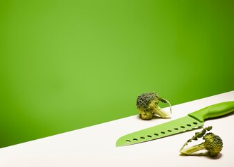 Artistic composition of broccoli and a green knife on a white surface against a green wall