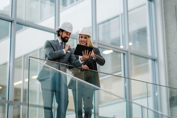 Smiling architects using tablet in modern building hallway