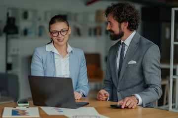 Business colleagues collaborating on laptop with charts and graphs in modern office