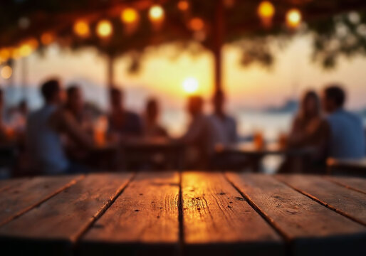 Empty rustic wooden table with copy space in pub. Background of blurred people sitting outdoor at sunset,  warm, moody atmosphere. Summer and vacation vibes.