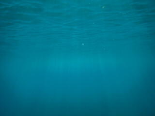 Dark blue ocean surface seen from underwater. Abstract waves underwater and rays of sunlight shining through, Sun light rays undersea deep, Underwater background with sea bottom, Mediterranean sea.