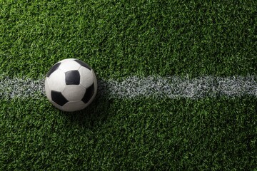 Overhead view of a classic black and white soccer ball resting on a vibrant green artificial turf field, next to a crisp white sideline