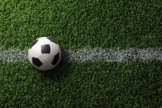 Overhead view of a classic black and white soccer ball resting on a vibrant green artificial turf field, next to a crisp white sideline - Powered by Adobe