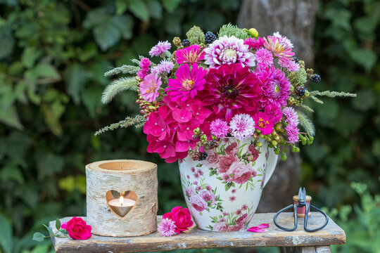 Blumen-Arrangement mit pink Dahlien, Hirtensienbl&uuml;ten, Zinnien und Federnelken in einer Tasse im Garten