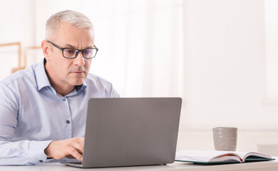 Web Surfing Concept. Focused Senior Man In Specs Using Wifi Working On Laptop, Free Space