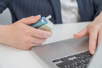 Business woman smoking an electronic cigarette while working on a laptop. Tobacco heating system. 