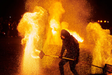 Silhouette of two fire performers with sparkling fire staff erupting in night sky, showcasing...