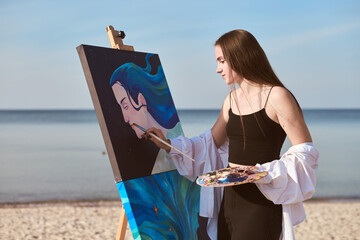 Young female artist stands on tranquil beach, intently painting portrait. Calm sea and open sky set...