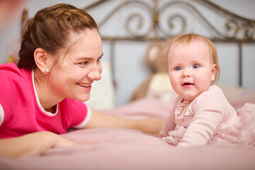 Young woman with brown hair, smiling baby girl indoors. Warm pink tones, soft lighting, metal...