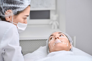 Beautician applies rejuvenating facial treatment to young woman. Soothing ambiance promotes...