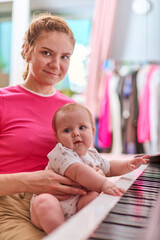 Young adult woman with tied-back hair and her baby girl engage with black and white synthesiser...