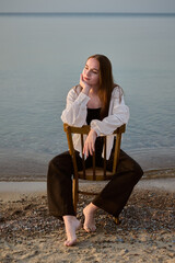 Young woman sits on chair facing sea, exuding calmness and tranquility. Serene beach setting at...