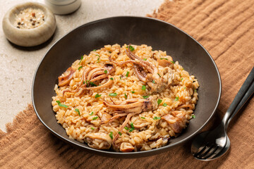 Risotto with squid or calamari, or totano with  tentacles. Italian seafood meal in a brown plate.  Brown table with textile runner.