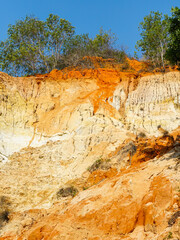Layered Sandstone Cliffs with Vegetation in Ham Tien Canyon, Vietnam under a Clear Blue Sky
