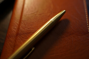 Elegant Golden Pen Resting on a Stylish Brown Leather Notebook