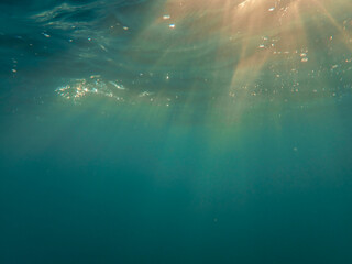 Fototapeta premium Dark blue ocean surface seen from underwater. Abstract waves underwater and rays of sunlight shining through, Sun light rays undersea deep, Underwater background with sea bottom, Mediterranean sea.