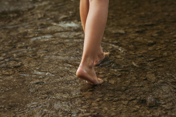 Horizontal shot of child's leg in the water. Walking barefoot in water of lake reservoir, lake embankment. Space for text