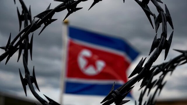 North korean flag waving in the wind behind rolls of barbed wire against a cloudy sky, symbolizing isolation, political boundaries, and restricted access