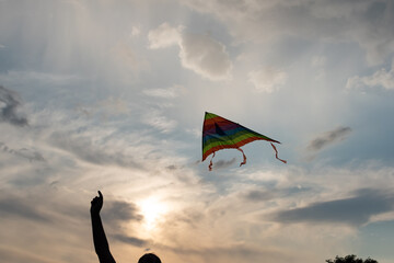 A girl flies a kite into the sky at sunset. A colorful kite soars through the sunset sky.