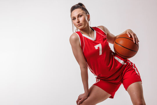 Dynamic female basketball player in red uniform posing with ball, confident sportswoman portrait