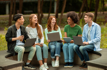 Diverse Multicultural Students Studying Outdoors With Different Electronic Devices, Sitting...