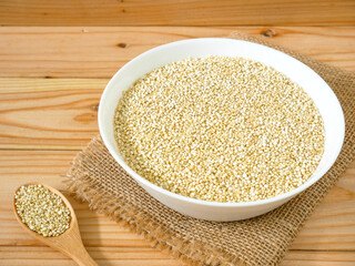 A bowl of uncooked white quinoa on wooden table