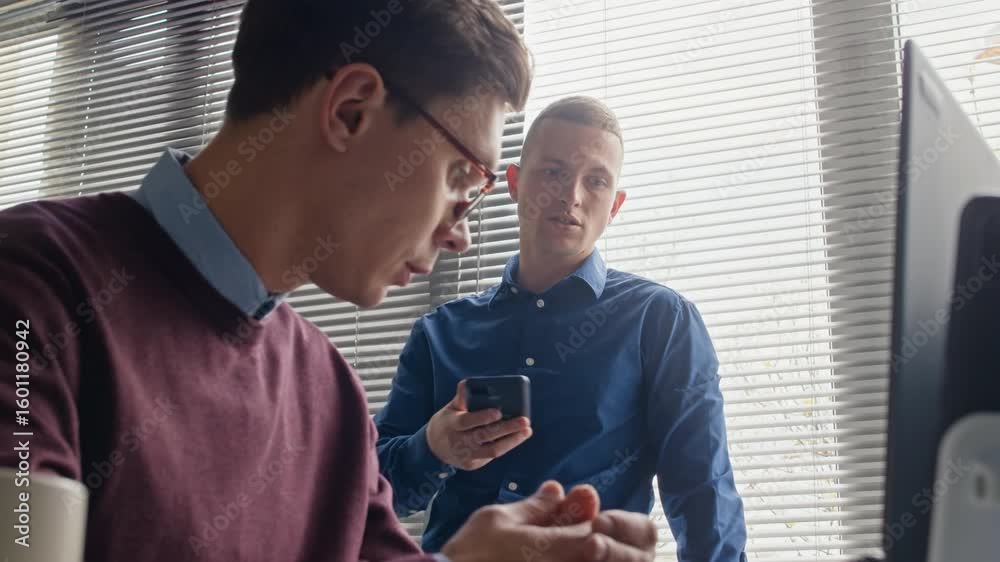 Wall mural focused male office worker with smartphone in hands talking to colleague debating work strategies wh