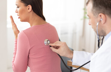 Pneumology Consultation Concept. Male specialist examining coughing female patient in clinic