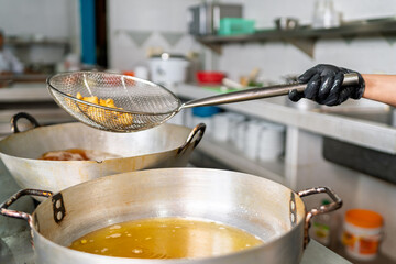 Chef frying fish in wok with hot oil in restaurant kitchen