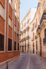 Charming narrow street in Valencia featuring traditional Spanish architecture, with decorative balconies and sunlight illuminating the vibrant buildings, creating a serene urban atmosphere.