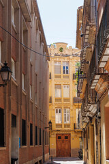 Fototapeta premium Scenic view of a narrow street in Valencia, showcasing beautiful architecture, sunlight, and contrasting building styles capturing the essence of urban life.