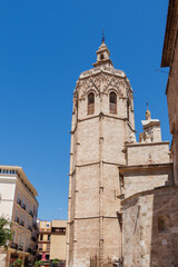 Obraz premium Historic bell tower in Valencia under a clear blue sky, surrounded by charming buildings, showcasing Gothic architecture and cultural landmarks, ideal for tourism.
