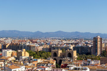 Obraz premium Aerial view of Valencia featuring urban landscapes and the iconic Torres de Serranos. The scene captures the vibrant city life under clear blue skies, perfect for travel themes.