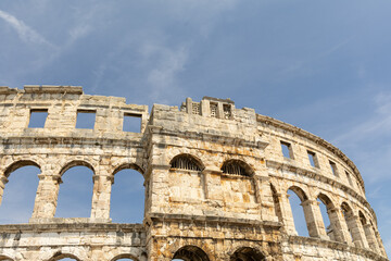 Fototapeta premium Ancient amphitheater structure showcasing weathered stone, arches, and blue sky, representing historical architecture and cultural heritage