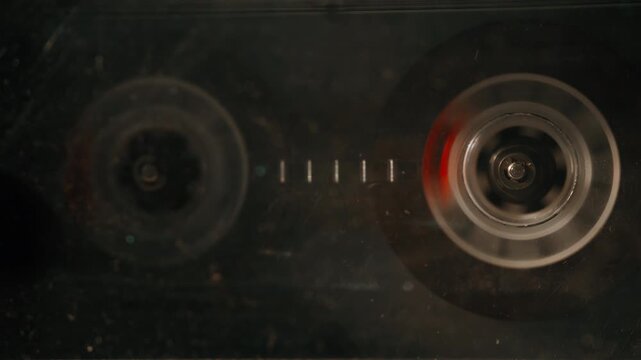 Macro magnetic tape turning steadily inside transparent cassette shell closeup.