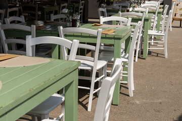 Summer cafe scene featuring green and white wooden tables and chairs arranged neatly under bright sunlight, creating a vibrant outdoor dining atmosphere