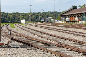 Railway tracks curving through an industrial area, with gravel and surrounding greenery,...
