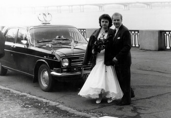 Vintage portrait of bride and groom on their wedding day near the car on the river bank. Retro...
