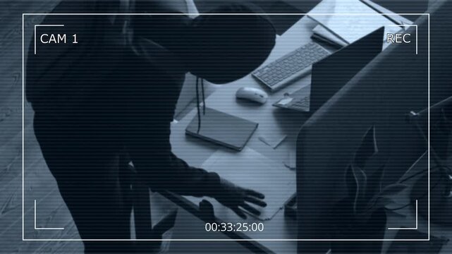 Security camera footage of two masked male criminals searching for confidential data rummaging through documents and installing spyware on corporate laptop at office, data breach concept