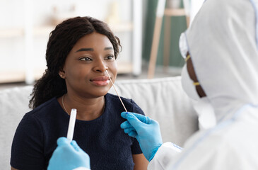Young black woman patient having PCR test at home, closeup. Unrecognizable doctor in protective...